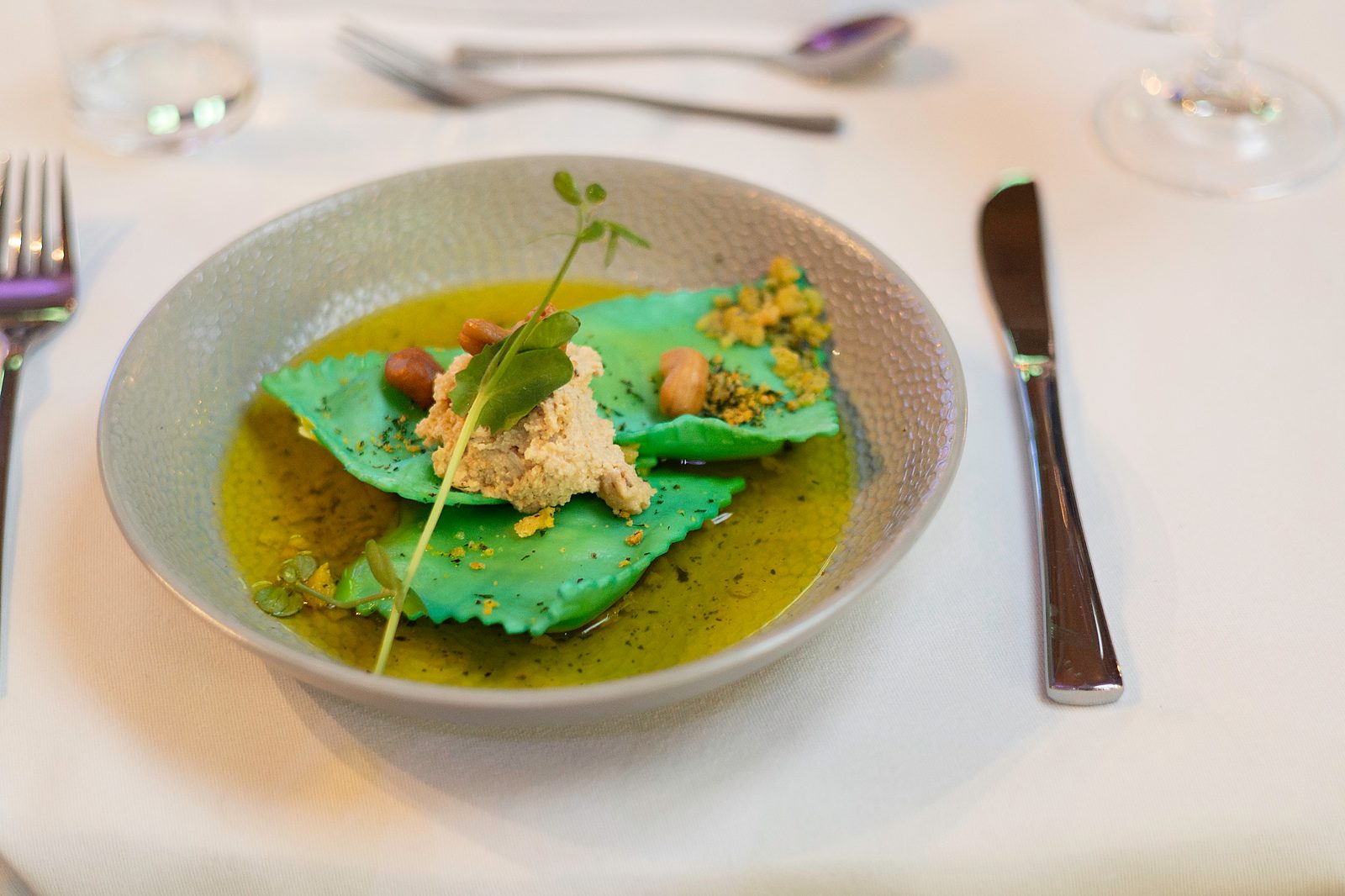 Groene ravioli met cashewnoten in olie aan een gedekte tafel tijdens een sitting dinner van KOM Catering